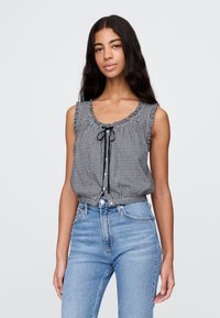 Svart-hvitt gingham ermeløs bluse med volangdetalj ved halsen og snøring, kombinert med høytlivs lyseblå jeans.