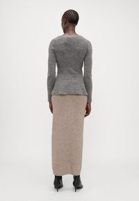 Grå strikket genser med lange ermer og en tettsittende peplumform. Kombinert med en beige, ankellang strikket skjørt. Svart hæl støvler.
