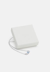 Collana d'argento con tre pietre preziose: due trasparenti e una azzurra chiara, poggiata accanto a una scatola bianca per gioielli con design in rilievo.