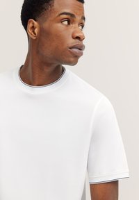 Weißes T-Shirt mit kurzen Ärmeln und Rundhalsausschnitt, das einen dezenten marineblauen Besatz um den Kragen und die Ärmel hat; glatte Stoffstruktur.