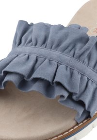 Blauwe suede slide sandaal met een gerimpelde band, een zachte beige voetbed en een witte zool met een bruine accent.