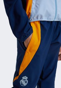 Navy and orange athletic tracksuit featuring a zippered jacket and elastic waistband, with a logo detail on the bottom left.
