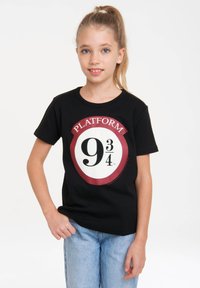 Black cotton t-shirt featuring a white circle and red border with "PLATFORM 9¾" and a large "9¾" print in black. Worn with light blue jeans.