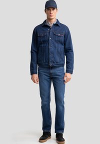 Jeans jakna v temno modri barvi, z sprednjimi žepi in gumbi. Ujemajoče temno modre kavbojke in črne teniske.