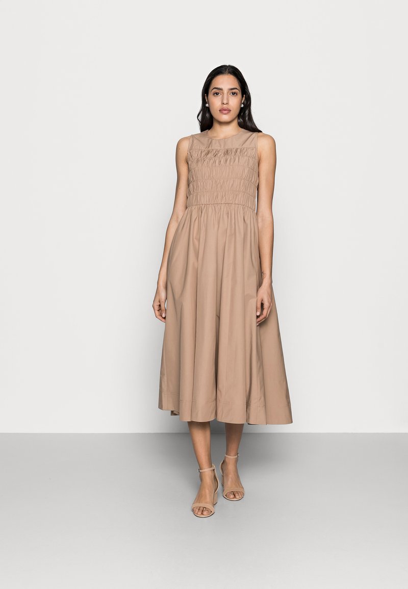 Beige, ärmelloses Kleid mit gerafftem Oberteil, fließendem Rock und mittellanger Schnittführung. Glattes Gewebe und subtile Struktur im gesamten Kleid.