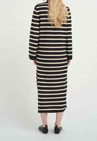 Svart och krämfärgad randig klänning med långa ärmar, med sidoflikar och figursydd siluett. Mjuk stickad material, knälängd design.