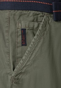 Olivgrüne Cargo-Hosen mit einem strukturierten marineblauen Gürtel. Merkmale sind gestickte Details und ein kleines Markenschild an der Fronttasche.