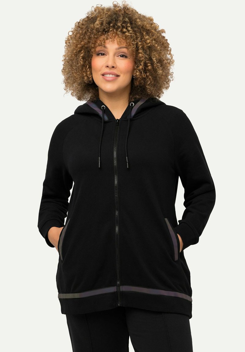 Sudadera negra con cremallera, capucha con cordón, bolsillos laterales y un acento a rayas en contraste en el dobladillo. Tejido suave y corte relajado.