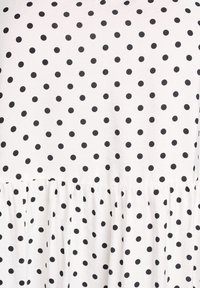 Mustad täpid valgel kangal, millel on volditud ääreline. Tekstuur näib siledana, kerge ja pehme viimistlusega.