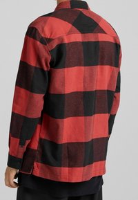 Camicia in flanella a quadri rossa e nera con colletto a bottoni e maniche lunghe, caratterizzata da un tessuto leggermente strutturato e un orlo dritto.