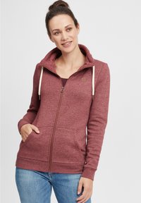 Sweat à zip rouge avec un col montant, des cordons de serrage et des poches avant. Fabriqué en tissu texturé, avec des poignets et un ourlet côtelés.