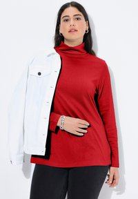 Červený dlouhý rolák z měkké látky, doplněný bílou džínovou bundou. Disponuje jednoduchým designem s jemnou texturou.