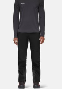 Zwarte outdoorbroeken met een slim fit, voorzien van een gestructureerd paneel op het onderste deel van het been, gecombineerd met een lange mouwen grijs shirt. Logo zichtbaar op de borst.
