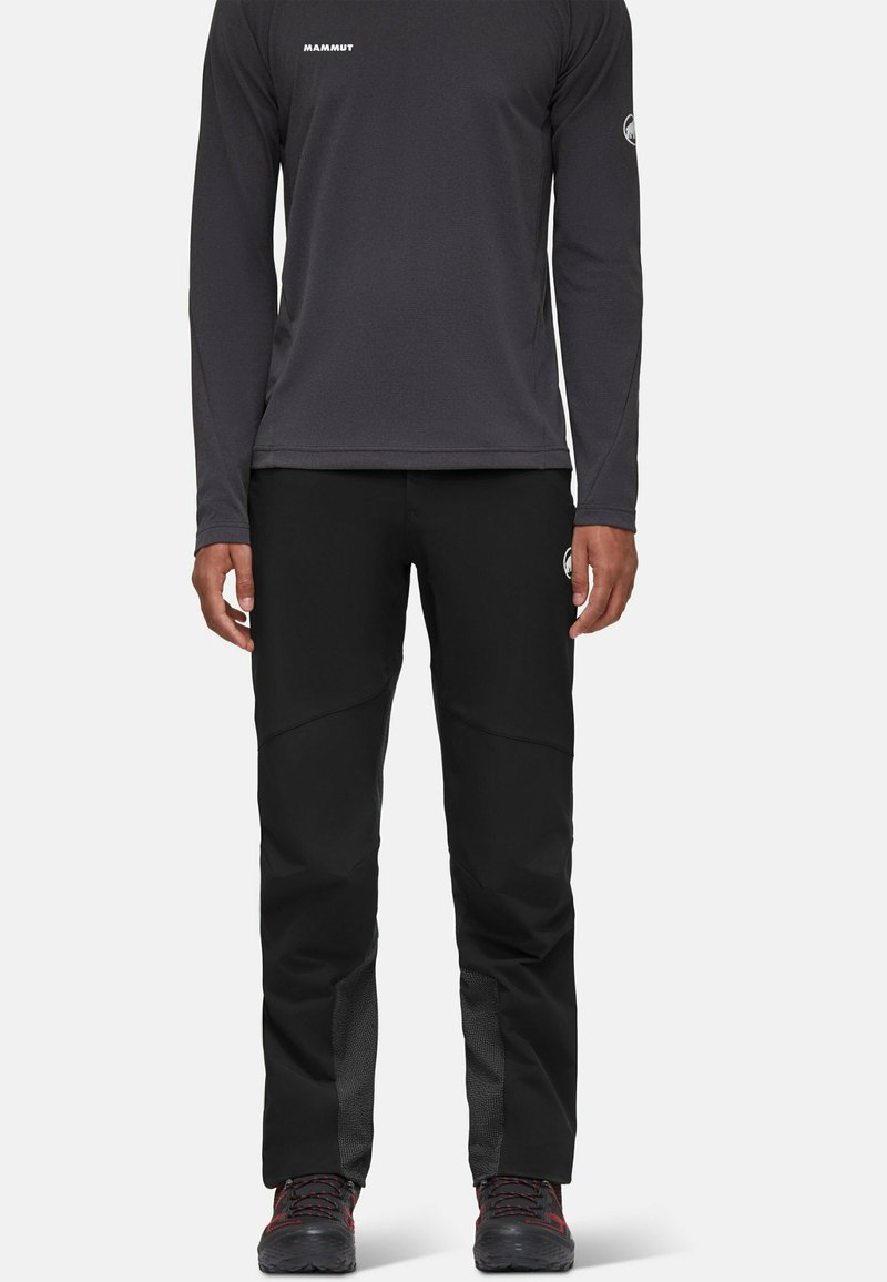 Zwarte outdoorbroeken met een slim fit, voorzien van een gestructureerd paneel op het onderste deel van het been, gecombineerd met een lange mouwen grijs shirt. Logo zichtbaar op de borst.