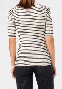 Rückansicht einer Person, die ein eng anliegendes, geripptes weißes Oberteil mit schwarzen horizontalen Streifen und schwarze Jeans trägt.