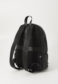 Sac à dos noir avec un extérieur texturé, des panneaux en maille et des bretelles ajustables. Il possède une poche zippée et des éléments de design élégants.