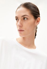 Witte katoenen T-shirt met een ronde hals, gladde textuur, ontspannen pasvorm, getoond op een model met een strakke vlechtstijl.