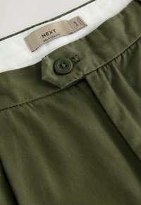 Olive green relaxed fit trousers with a button closure, featuring a soft texture and a white lining along the waistband. Brand label visible.