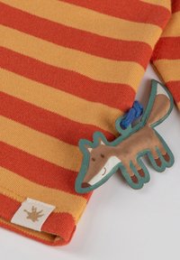 Gestreifter orange- und gelber Stoff mit einer weichen Textur zeigt eine Applikation eines braunen Fuchses sowie ein kleines Etikett mit einem Handabdruckdesign.