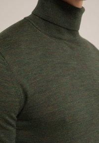 Temnozeleni pleteni pulover s turtleneck ovratnikom. Gladka tekstura, prilegajoča zasnova, ki poudarja doslednost v barvi in materialu.