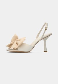 Μπεζ ψηλοτάκουνα με αναδιπλούμενη φτέρνα και γυαλιστερή φινίρισμα, με μια μεγάλη λεπτομέρεια από σατέν φιόγκο και ένα λεπτό, κωνικό ψηλό τακούνι. Σχεδίαση με ανοιχτή μύτη.