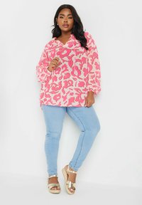 Blusa con motivo floreale rosa, con cappuccio a coulisse, maniche lunghe e vestibilità morbida, abbinata a jeans azzurri e sandali espadrillas dorati.