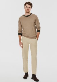 Beżowy sweter robiony na drutach z ciemnozielonymi akcentami, w zestawie z jasnobeżowymi spodniami oraz brązowymi botkami za kostkę; charakteryzuje się prostym krojem i dopasowanym fasonem.