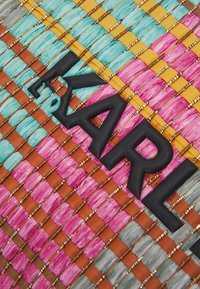 Woven textile featuring pink, turquoise, orange, and gray strands with metallic accents; "KARL" logo in matte black positioned prominently.