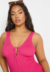 Fuchsia-ribbade baddräkt i ett stycke med djup V-ringning, nyckelhål på bröstet och tjocka remmar. Slät textur och figurnära design.