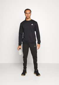 Set di felpa e pantaloni neri realizzato in misto cotone. La felpa presenta un collo tondo e un piccolo logo bianco; i pantaloni hanno strisce laterali bianche.