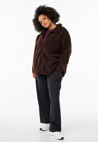 Braune, flauschige Fleecejacke mit Reißverschluss und Stehkragen. Kombiniert mit schwarzen Hosen und weißen Turnschuhen für einen lässigen Look.