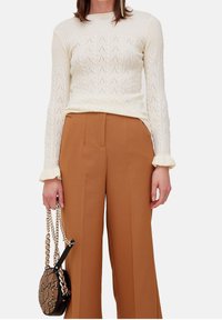 Kremowy sweter dzianinowy o teksturowanym wzorze, zestawiony z brązowymi, szerokimi spodniami o wysokim stanie. Stylizację uzupełnia torebka w czarno-wężowy wzór.