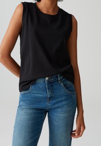 Un haut sans manches noir en tissu doux, associé à un jean taille haute bleu clair. Le haut présente un col arrondi et une coupe décontractée.