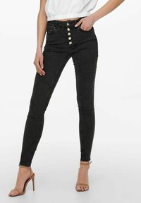 Jeans skinny negros con cintura alta, que cuentan con un cierre delantero de botón y cinco bolsillos. La tela tiene un acabado suave y ligeramente texturizado.