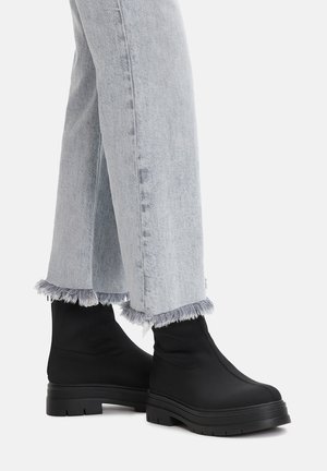 Czarne botki za kostkę wykonane z gładkiego materiału z teksturowaną podeszwą. Połączone ze jasnoniebieskimi dżinsami z postrzępionymi brzegami.