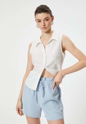Witte linnen mouwloze blouse met kraag en knopen aan de voorkant, gecombineerd met lichtblauwe shorts met trekkoord, met een ontspannen pasvorm.
