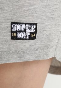 Harmaa kangas, jossa on teksturoitu pinta, ja mustavalkoinen etiketti, jossa lukee "SUPER DRY" ja vuosi "54" kullanvärisinä.