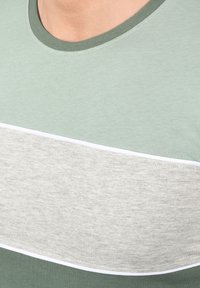 Grøn bomulds t-shirt med en grå vandret stribe, der har en rund hals og kontrasterende hvid kant. Glat tekstur og enkelt design.