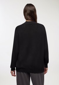 Maglione nero a maglia con scollo rotondo, maniche lunghe e vestibilità ampia. Texture liscia con dettagli a coste sui polsini e sull'orlo.