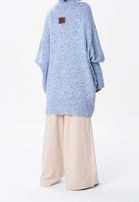 Oversized ljusblå stickad tröja med vida ärmar och ribbad nederkant, kombinerad med cremefärgade vida byxor med ränder. Brun läderetikett på baksidan.