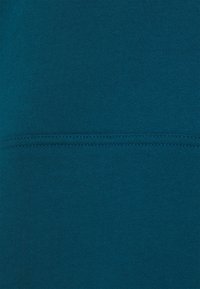 Tela de algodón azul verdoso con textura suave y detalle de costura horizontal. Presenta un color uniforme con ligera elasticidad.