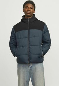 Padded jacket featuring a navy body with a black upper panel, full zip, and hood. Textured fabric with horizontal stitch detailing.