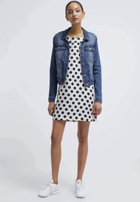 Denim jacket with metal buttons over a white and black polka dot dress, paired with white sneakers. Smooth fabric and classic silhouette.
