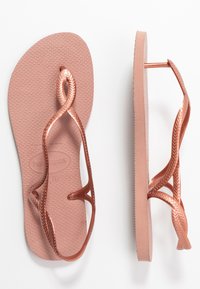 Chinelo em rosa dourado com sola de borracha texturizada e design de tiras trançadas. Apresenta uma superfície lisa e uma tira reforçada para durabilidade.