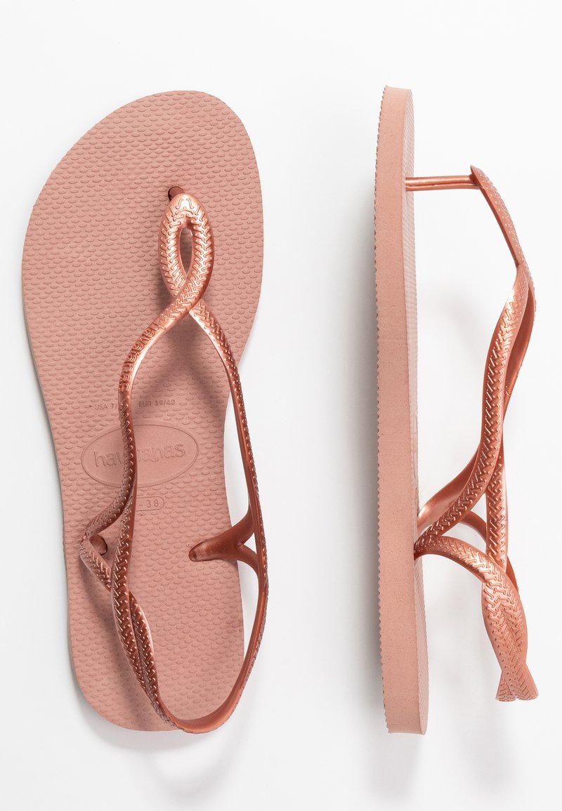 Chinelo em rosa dourado com sola de borracha texturizada e design de tiras trançadas. Apresenta uma superfície lisa e uma tira reforçada para durabilidade.