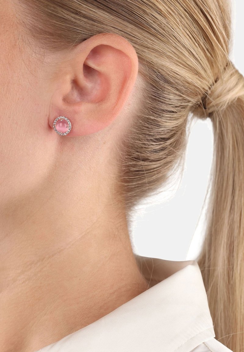 Pendientes de studs redondos con un centro de piedra rosa, rodeado por un halo de piedras de rhinestone transparentes, montados en metal de tono plateado.
