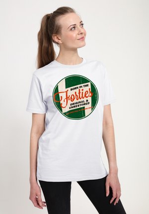 Ung kvinde med hestehale iført en hvid t-shirt med teksten "Født i fyrrerne, original og urestaureret," der kigger op mod højre.