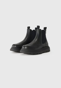 Pair of black leather Chelsea boots with elastic side panels and thick rubber soles on a light gray background.