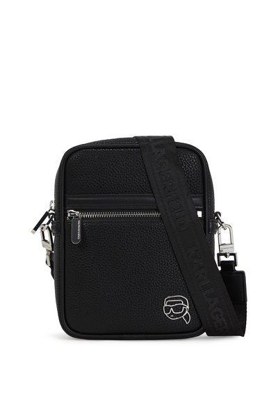 Sac bandoulière noir en texture avec une fermeture éclair, une sangle ajustable et quincaillerie en argent. Présente un détail de logo à l'avant.