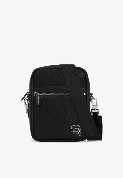Sac bandoulière noir en texture avec une fermeture éclair, une sangle ajustable et quincaillerie en argent. Présente un détail de logo à l'avant.